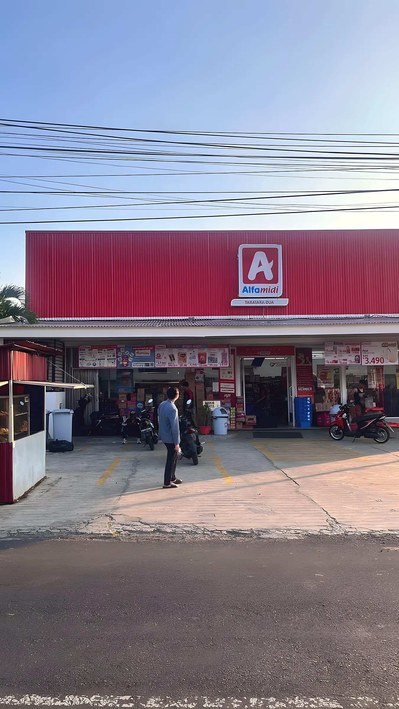 Minimarket Alfamidi Taratara Dua dengan fasad merah di tepi jalan utama